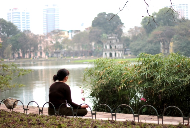 a woman meditating near Hoan Kiem lake in the morning